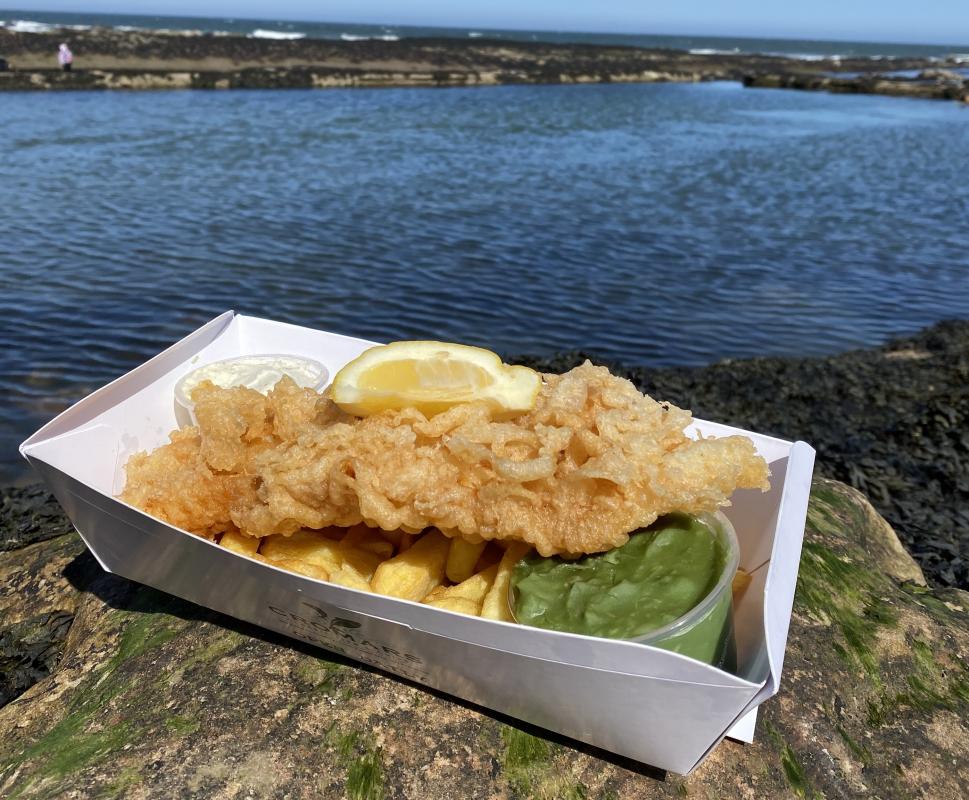 A portion of Cromars fish and chips with mushy peas sitting on a rock by the sea